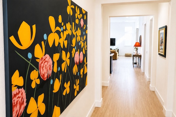 A hallway with a large abstract painting on the left, a dining area with a table and chairs, and a framed picture on the wall. - Thoughtfully Designed Lodi Retreat - Fire Pit • Putting Green • Near Wineries (Lodi)