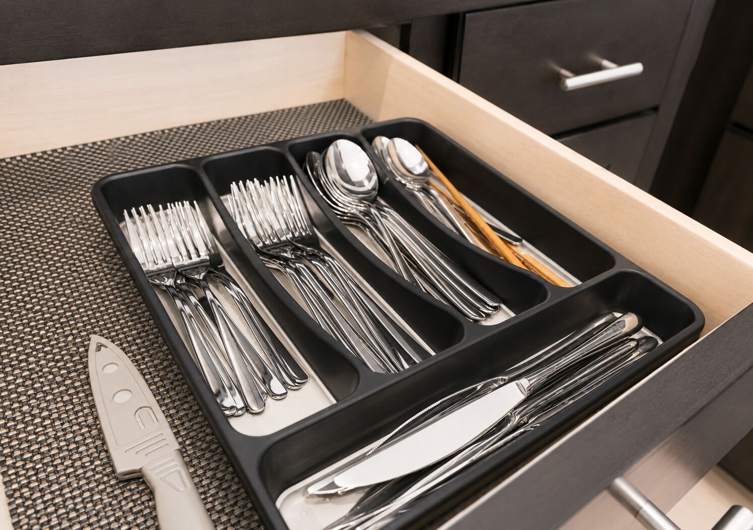 Un cajón con divisores que contiene varios utensilios, incluyendo tenedores, cucharas y un cuchillo.