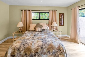 Ein Schlafzimmer mit einem Bett, zwei Nachttischen, einem Fenster mit Vorhängen und einem Wandbild.