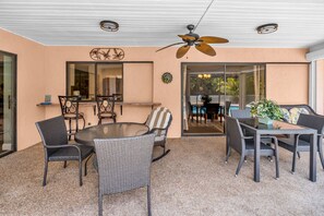 Eine Terrasse im Freien mit einem runden Tisch und Stühlen, einem Deckenventilator und Blick auf einen Pool durch Glasüren.