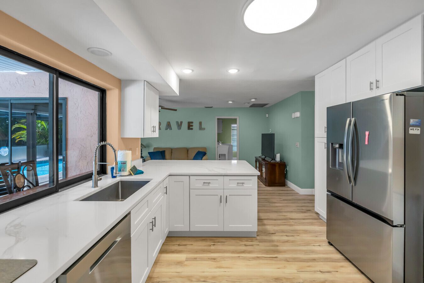 A modern kitchen with white cabinets, a stainless steel refrigerator, and a view of a swimming pool.