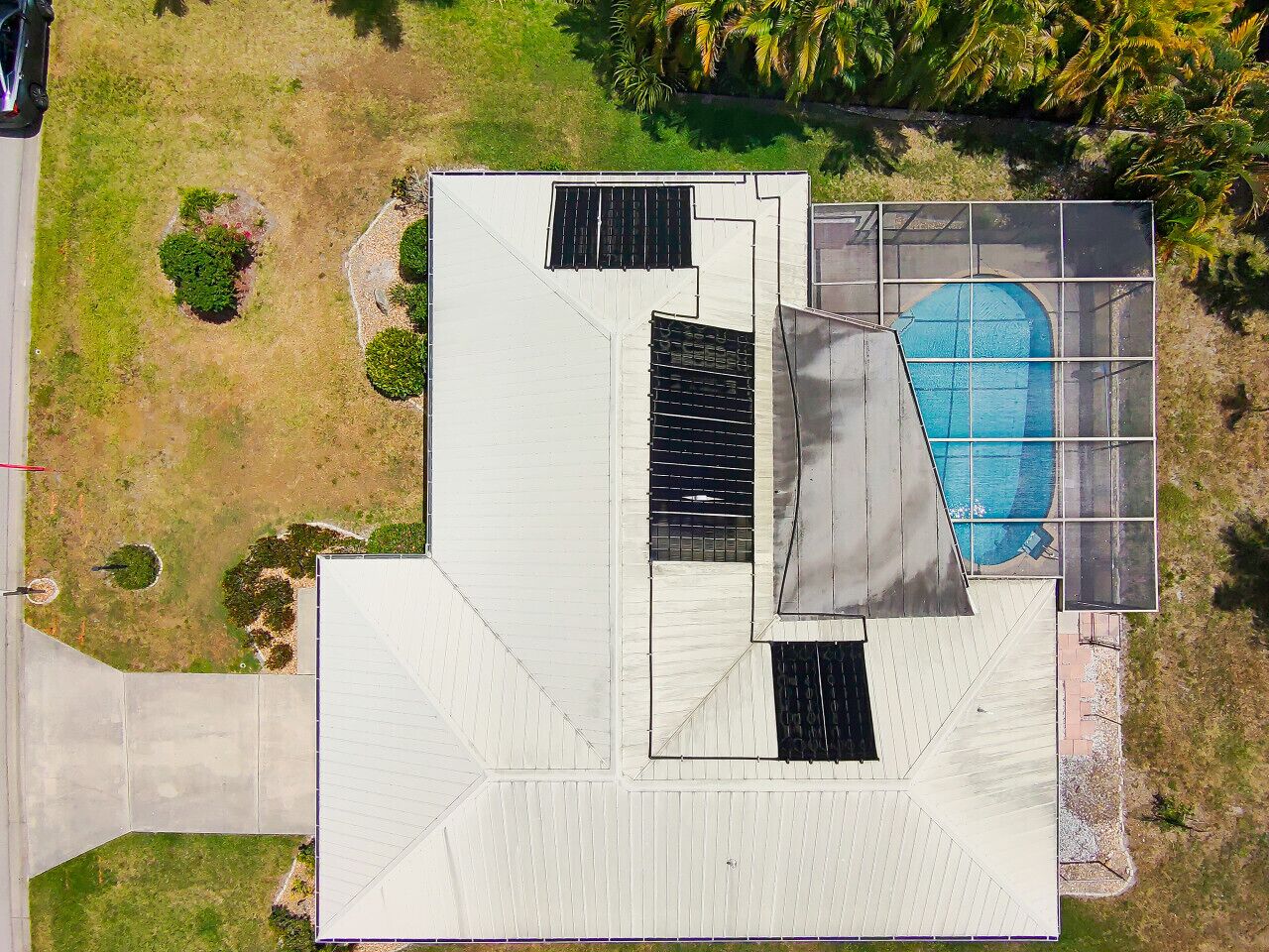 An aerial view of a modern building with a swimming pool, a covered patio, and a landscaped area with trees and shrubs.
