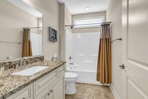 Une salle de bain avec un double lavabo, des toilettes, une baignoire et un rideau de douche.