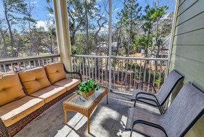 A balcony with a sofa, a wicker table with a plant, and two chairs. - Sunnyside Village-3A condo near Marshwalk with pool (Murrells Inlet)