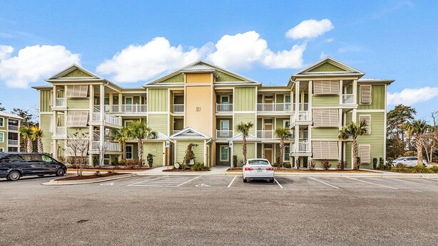 A multi-story hotel with a central entrance, balconies, and a parking lot. - Sunnyside Village-3A condo near Marshwalk with pool (Murrells Inlet)