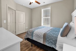 Une chambre à coucher avec un lit, un ventilateur de plafond, une fenêtre avec des stores et une porte.