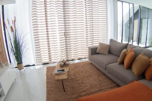 Ein modernes Wohnzimmer mit einer Couch, einem Couchtisch und einem großen Fenster mit gestreiften Vorhängen.