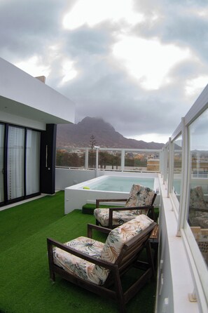 Eine Dachterrasse mit Pool, zwei Liegestühlen und Blick auf einen Berg.