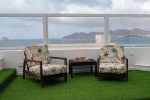 Ein Zimmer mit zwei Sesseln, die zu einem großen Fenster mit Blick aufs Meer hin ausgerichtet sind.