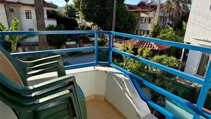 Un balcó amb una cadira de plàstic verd, una barana blava i vistes a edificis i arbres de l'entorn.