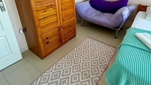 Un dormitori amb un armari de fusta, un llit amb colcha quadres verda i blanca, un almoïna morada i una catifa estampada.