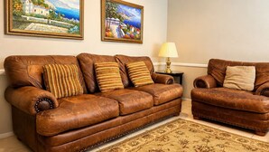A brown leather sofa with striped cushions, a matching armchair, a small table with a lamp, and two framed landscape paintings on the wall. - Casa Avalon Hotel (Avalon)