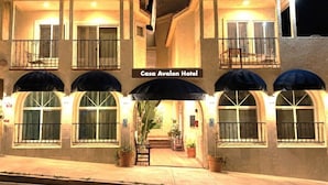 Un hotel con un cartel que dice 'Casa Avalon Hotel', que presenta una entrada central con un corredor cubierto, plantas en macetas y un balcón con barandilla.