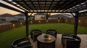 Eine Terrassengruppe im Freien mit einer Pergola, einem runden Tisch mit Stühlen und einem kleinen Topfpflanzen.
