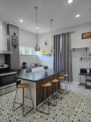 A modern kitchen with a central island, bar stools, pendant lighting, and a chalkboard sign. - Beautiful two minutes from Alamodome and all downtown fun (San Antonio)