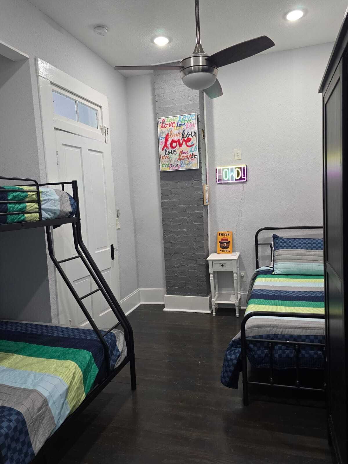 Une chambre avec des lits superposés, un ventilateur de plafond, une lampe fixée au mur et une affiche motivante.