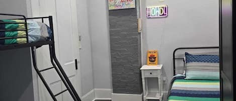 Une chambre avec des lits superposés, un ventilateur de plafond, une lampe fixée au mur et une affiche motivante.