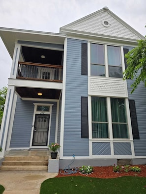A two-story house with a front porch, a balcony on the upper floor, and a small garden area. - Beautiful two minutes from Alamodome and all downtown fun (San Antonio)