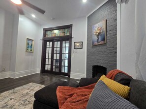 A living room with a dark wood door, a fireplace, and a gray brick accent wall. - Beautiful two minutes from Alamodome and all downtown fun (San Antonio)