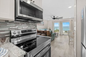 A modern kitchen with a built-in oven and microwave, a dining area with a view of the ocean, and a balcony with a ceiling fan. - Summit Unit 422 Gulf Front 1 Bedroom/Bunks (Panama City Beach)