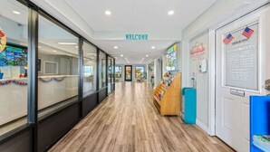 Un pasillo de hotel con un cartel de 'WELCOME', una recepción y un tablón de anuncios con una bandera estadounidense.