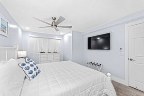 Ein Schlafzimmer mit einem Bett, einem Deckenventilator, einem an der Wand montierten Fernseher und einer weißen Tür.