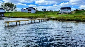 A waterfront property with a dock extending into a body of water, surrounded by grassy areas and multiple houses. - Lakefront Escape | Private Pool + Dock Access (Mineral)