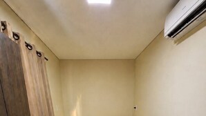 A small, single-bed room with a wooden wardrobe, a bed with a brown blanket, and an air conditioning unit on the wall. - HOTEL IDEAL 2 (Inocencia)