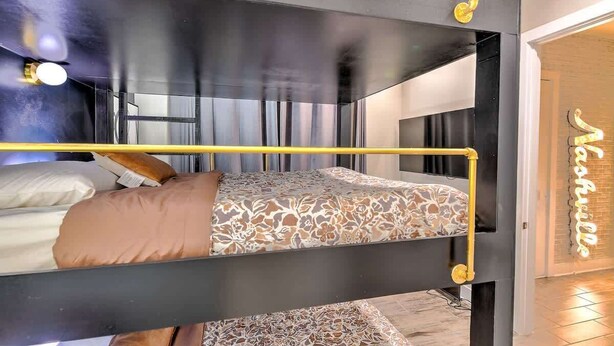Ein Stockbett mit gemustertem Bettbezug, einem Kopfteil und einem Neonzeichen im Hintergrund.