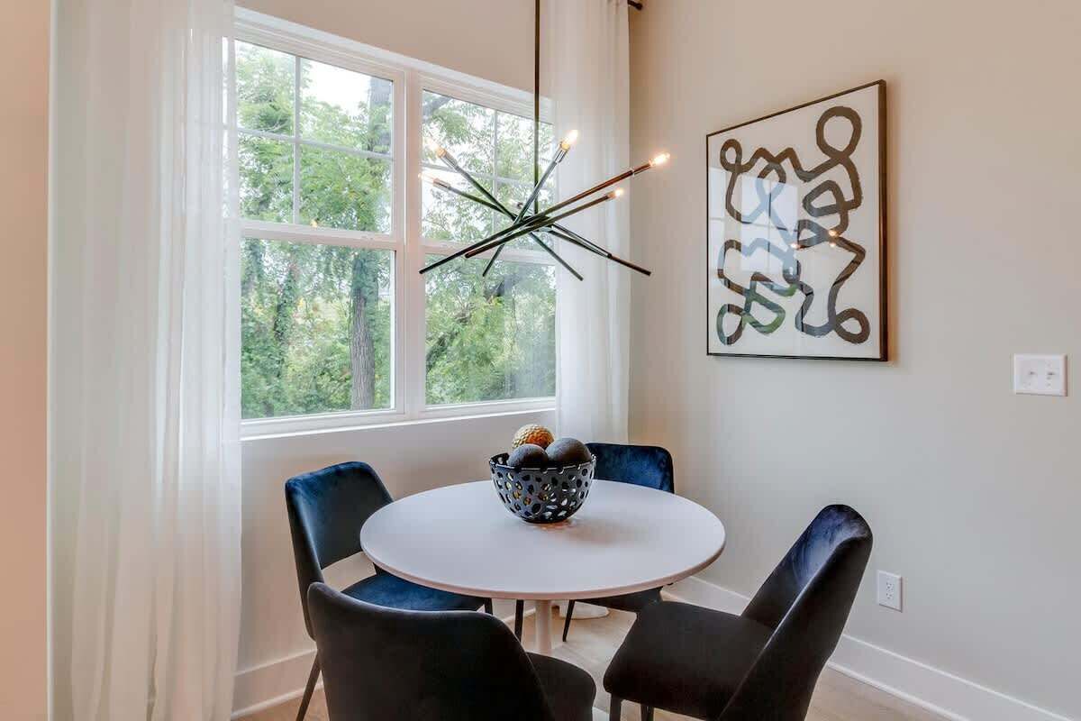 A dining area with a round table, four chairs, a modern chandelier, and a piece of abstract art on the wall.