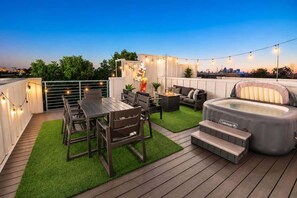 Eine Terrasse im Freien mit Holzboden, künstlichem Rasen, einem Esstisch mit Stühlen, einer Couch, einem Whirlpool und Lichterketten.