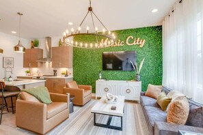 Ein modernes Wohnzimmer mit grüner Wand, einer Kronleuchter, einer Couch, einem Couchtisch und einem Fernseher.