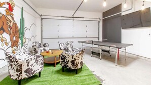 Ein Zimmer mit Tischtennisplatte, zwei Stühle mit Kuhmuster, einem kleinen runden Tisch und einem Wandbild.