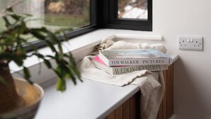 Ein Fenster mit Blick auf einen Garten, eine Topfpflanze und zwei Bücher auf einem Fensterbrett.