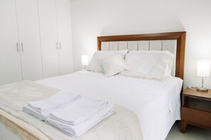 A neatly made bed with pillows, a bedside lamp, and a stack of towels on a wooden nightstand. - Newly Renovated 2BR Apartment (Lince)