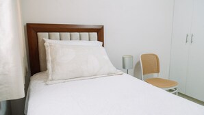 A bed with a wooden headboard, a white pillow, and a white bedspread. There is a wicker chair with a lamp beside the bed. - Newly Renovated 2BR Apartment (Lince)