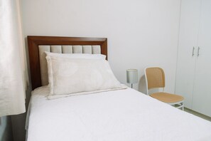 A bed with a wooden headboard, a white pillow, and a white bedspread. There is a wicker chair with a lamp beside the bed. - Newly Renovated 2BR Apartment (Lince)