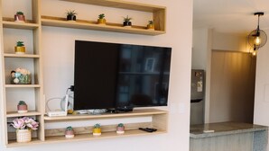 A living room with a flat-screen TV, a sofa, a small table, and a kitchen area in the background. - Newly Renovated 2BR Apartment (Lince)