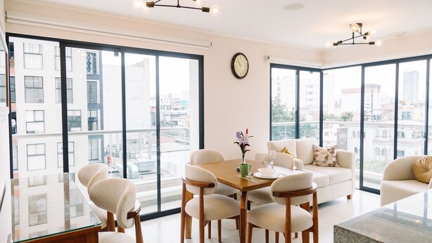 A modern living room with a dining table, chairs, a sofa, and large windows offering city views. - Newly Renovated 2BR Apartment (Lince)