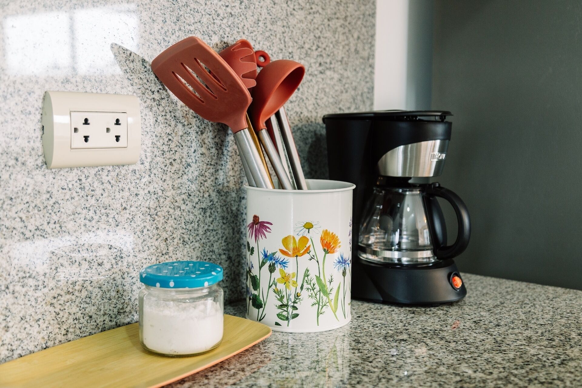 A kitchen counter with a coffee maker, a jar of sugar, and a mug with floral designs.