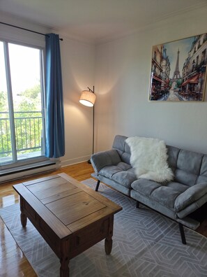 Un salon avec un canapé, une table basse, un lampadaire et un tableau représentant une rue de Paris.