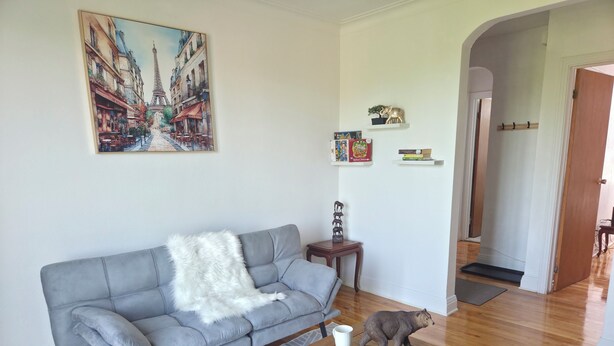 A living room with a grey sofa, a wooden coffee table, a painting of Paris, and a small bear figurine. - Modern 2BR • Steps to Jean-Talon Metro • Fast Wi-Fi • Long Stays Welcome (Montréal)