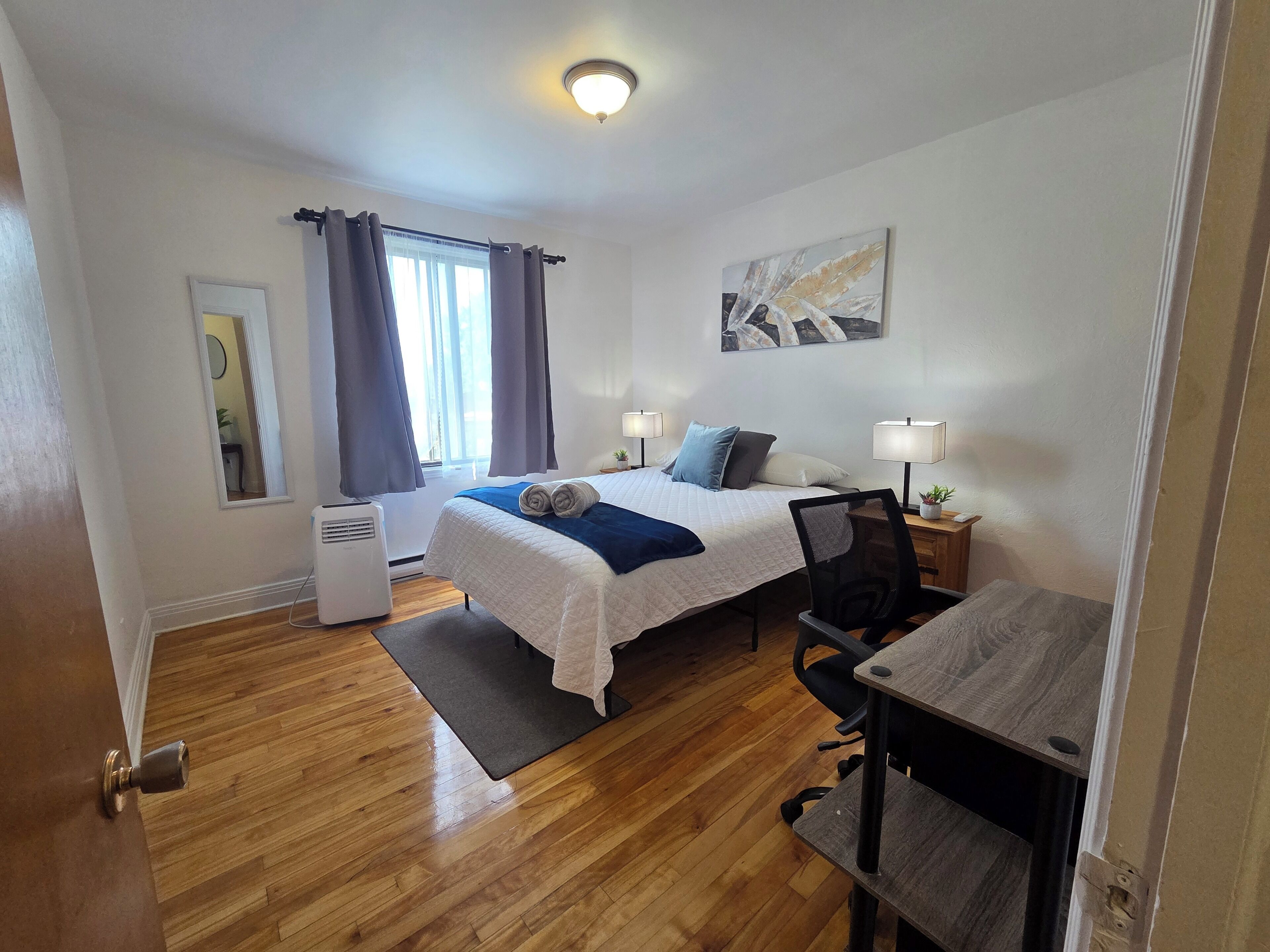 Habitación de hotel con cama, escritorio, silla, lámparas de noche y ventana con cortinas.