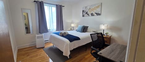 Hotellihuone, jossa on sänky, työpöytä, tuoli, yöpöytälamput ja ikkuna, jossa on verhot.