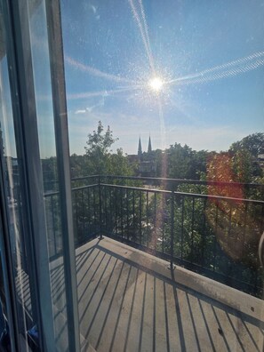 Ein Balkon mit Metallgeländer, wolkenloser Himmel und Blick auf ein entferntes Gebäude mit zwei Türmen.