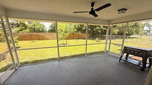 A covered patio with a ceiling fan, a barbecue grill, and a view of a grassy yard. - Charming 3-bedroom house with AC in Sunny Cape Coral (Cape Coral)