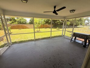 A covered patio with a ceiling fan, a barbecue grill, and a view of a grassy yard. - Charming 3-bedroom house with AC in Sunny Cape Coral (Cape Coral)