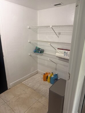 A laundry room with metal shelves, a tiled floor, and cleaning supplies. - Charming 3-bedroom house with AC in Sunny Cape Coral (Cape Coral)