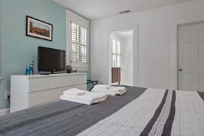 Ein Schlafzimmer mit einem Bett, einem Fernseher auf einer Kommode, einem Fenster und einer Tür.