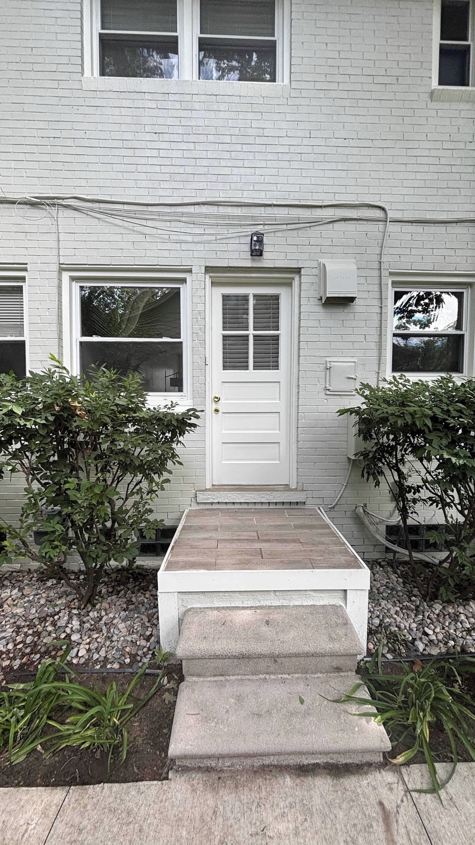 A white brick building with a front door, two windows, and a small porch with steps.